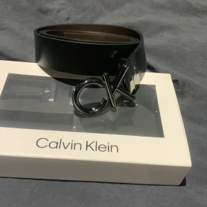 Svart bälte från Calvin Klein - Snyggt svart bälte från Calvin Klein med en stilren CK-logga på spännet. Perfekt för att ge en elegant touch till din outfit. Bältet kommer i en elegant förpackning.
