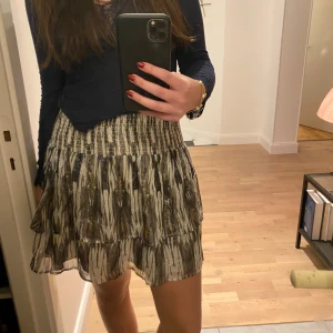 Mönstrad kjol med volang - Säljer en snygg mönstrad kjol med volangdetaljer. Kjolen har ett elastiskt midjeband och ett jättecoolt mönster! Perfekt för att ge en trendig touch till din outfit! Finns en defekt som syns på sista bilden men den syns inte alls med kjolen på💓