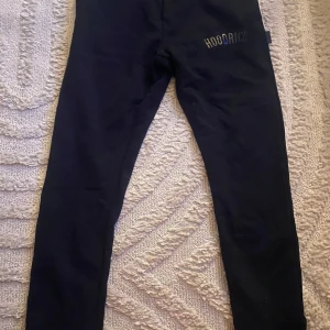 Svarta mjukisbyxor från Hoodrich - Snygga svarta mjukisbyxor från Hoodrich med snörning i midjan och logotyp på benet. Perfekta för en avslappnad stil. Byxorna har en bekväm passform och är tillverkade i mjukt material.