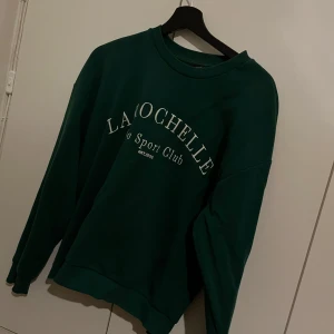 Grön sweatshirt från Gina Tricot - Säljer en snygg mörkgrön sweatshirt från Gina Tricot med texten 'La Rochelle Vélo Sport Club' tryckt på framsidan. Tröjan har en rund halsringning och långa ärmar, perfekt för en avslappnad stil. Passar bra till jeans eller leggings. Knappt använd, bra kvalitet inga fläckar. Skriv vid frågor💗