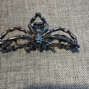 Hårklämma i form av en spindel - Unik hårklämma i metall med en cool spindeldesign. Klämman är i en mörk silverfärg och har en robust konstruktion som håller håret på plats. Perfekt för att ge din frisyr en edgy touch.