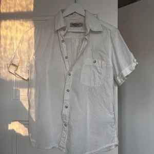 Vit linneskjorta från Dressmann - Säljer en stilren vit kortärmad skjorta från Dressmann i linneblandning. Perfekt för varma dagar med sin lätta och luftiga känsla. Hör av dig vid minsta fråga eller fundering!