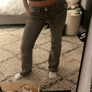 Grå jeansbyxor - Snygga grå jeansbyxor med låg midja och bootcut-stil. Perfekta för en avslappnad look. De har klassisk femficksdesign och knappar framtill.