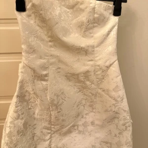Vit klänning/ Studentklänning  - Elegant vit bandeau klänning perfekt till studenten!! Den har ett litet mönster som man ser på nära håll. Klänningen har en stor rosett på baksidan. Perfekt för speciella tillfällen. 🩵🩵