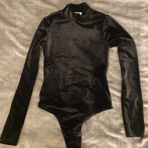 Svart sammet bodysuit från H&M - Snygg svart bodysuit i sammet från H&M med långa ärmar och polokrage. Perfekt för en elegant look. Passar bra till både kjol och byxor.