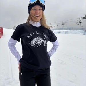 Marinblå t-shirt med bergsmotiv - Snygg mörkblå t-shirt med tryck av berg och texten 'AFTERSKI'. Perfekt för en avslappnad stil efter en dag i backen. T-shirten har en normal passform och korta ärmar.