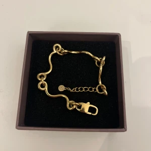 Guldarmband med vågig design från Edblad.  - Jag säljer det här eleganta guldarmbandet med unik vågig design. Armbandet har en justerbar kedja och ett stilrent lås. Perfekt för att ge en touch av lyx till din outfit. Helt oanvänd förutom vid bilden då. 