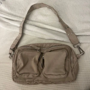 Beige axelväska med nitar - Beige handväska. Bandet är lite slitet (se bild). Men annars är väskan i bra skick.