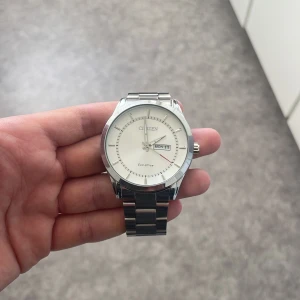 Citizen Eco-Drive herrklocka - Snygg Citizen Eco-Drive herrklocka med vit urtavla och dag/datumvisning. Armbandet är i rostfritt stål med en säker låsning. Perfekt för den som gillar stilren design och pålitlig funktion.