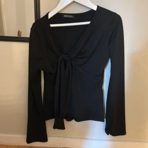 Svart långärmad topp från Missay - Snygg svart långärmad topp från Missay med knytning framtill. Perfekt för en stilren look. Toppen har en v-ringad design och är tillverkad i ett mjukt material. Använd 1 gång så den är i nyskick! Står att den är i xs-s men jag har xs i toppar och den här är för liten, den sitter mer som en xxs💓