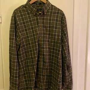 Rutig skjorta från GANT - Säljer en snygg rutig skjorta från GANT i gröna och röda toner. Skjortan har långa ärmar och knappar framtill. Perfekt för en stilren look.