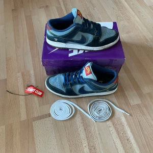 Nike SB Dunk Low 'Why So Sad?'🫐🦅 - 🔥Säljer ett par Nike SB Dunk Low 'Why So Sad?' sneakers. Köptes i new york för två år sedan och har används en del, vilket man ser på bilderna. Skorna är 7/10 skick, den enda riktiga ”skadan” syns på bilden, annars är de bara lite slitna/smutsiga. Jag försökte tvätta dem lite, men jag är säker på att det går att göra bättre. De är storlek 45,5 men passar mig perfekt som har 44/45.🔥Originalbox+Extrasnören medföljer, pris går att diskuteras🔥