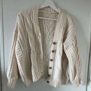 Beige/vit stickad kofta med knappar - Mysig beige/vit stickad kofta med ett vackert flätmönster och stora knappar framtill. 