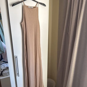Beige långklänning från Xside - Säljer en stilren beige långklänning från Xside. Klänningen har en ribbad textur och smala axelband, vilket ger en elegant look. Har dubbelt tyg för att inget ska synas igenom.  Perfekt för varma dagar eller sommarens fester. 💫