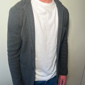 Stickad kavaj från Lexington - Snygg grå stickad kavaj med två knappar framtill och praktiska fickor. Perfekt för en stilren look. Passar bra över en t-shirt eller för en avslappnad stil.