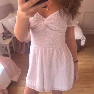 Vit kortklänning med knyt och puffärmar - Söt vit kortklänning med shorts inuti, fina puff ärmar och knyte där bak så att man kan få en fin passform vid midjan. Gulligt prickigt mönster. Inte använd vid något tillfälle då det ej passa mitt omtycke.