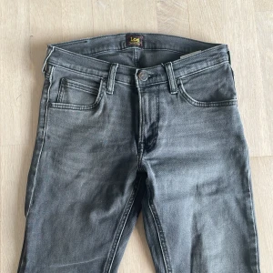 Grå jeans från Lee 28/30 - Snygga grå jeans från Lee med en klassisk femficksdesign. De har en straight passform och är tillverkade i ett slitstarkt denimtyg. Perfekta för en stilren look.
