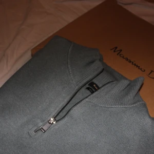 Grå halfzip från Massimo Dutti - Snygg grå tröja från Massimo Dutti med halfzip och ribbade muddar. Perfekt för en stilren look. Tröjan har en normal passform och är tillverkad i ett mjukt material.