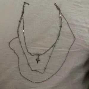 Dubbelradigt halsband med stjärnhänge - Snyggt dubbelradigt halsband i silverfärg med ett stjärnformat hänge. Kedjan har små dekorativa detaljer som ger en extra touch. 