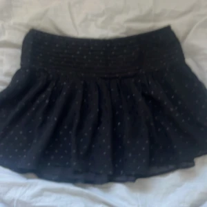 Svart prickig kjol från Gina Tricot - Säljer en söt svart kortkjol från Gina Tricot med små prickar. Kjolen har en bred resår i midjan för en bekväm passform. Perfekt för att ge en lekfull touch till din outfit!