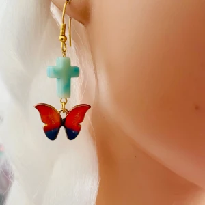 Made by prisförslag- 1 st Örhänge med kors och fjäril - Ett Unikt örhängen med ett ljusblått kors och en färgglad fjäril i rött och blått. Är fäst på en guldfärgad krok. Perfekt för att ge en färgklick till din outfit.