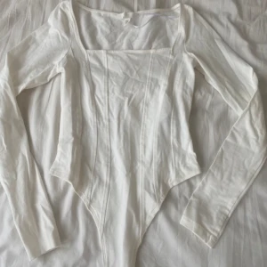 Vit långärmad bodysuit - Säljer en stilren vit långärmad bodysuit med fyrkantig halsringning. Perfekt för lager-på-lager eller att bära som den är. Den har en figurnära passform som framhäver silhuetten.