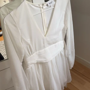 Vit klänning med v-ringning - Elegant vit klänning från bubbleroom med v-ringning och långa ärmar. Klänningen har en dragkedja i ryggen och knytning bak samt är i storlek 34. Den är endast använd en gång och tvättas innan den postas🌸 perfekt för student eller skolavslutning! (Säljer pga att jag endast använt den en gång under 3år)