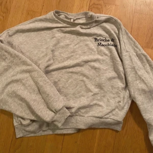 Grå sweatshirt från NLY Trend - Säljer en grå sweatshirt från NLY Trend med texten 'Brioche & Macchiato' broderad på bröstet. Tröjan har en avslappnad passform och långa ärmar, perfekt för en casual look. Mjuk och bekväm att bära.