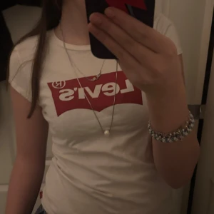 Vit t-shirt från Levi's - Säljer en klassisk vit t-shirt från Levi's med det ikoniska röda logotyptrycket på bröstet. T-shirten har en rund halsringning och korta ärmar. Perfekt för en avslappnad stil.