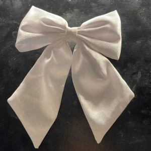 Vit rosett diadem - Elegant vitt diadem med stor rosett. Perfekt för att ge en stilren touch till din outfit. Tillverkad i ett mjukt och glansigt material som ger en lyxig känsla.
