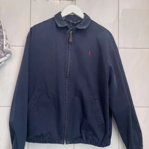 Mörkblå jacka från Polo Ralph Lauren - Säljer en stilren mörkblå jacka från Polo Ralph Lauren. Jackan har en dragkedja framtill och en liten röd broderad logotyp på bröstet. Bra skick. Perfekt nu till våren! Pris kan diskuteras.                                                     Mvh 