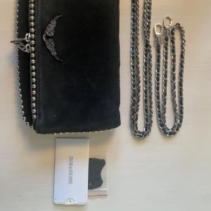 Svart axelväska med kedja från Zadig & Voltaire - Snygg svart axelväska i mocka från Zadig & Voltaire. Väskan har en  kedja som axelrem.jag säljer denna på grund av att jag har andra väskor ja använder💞