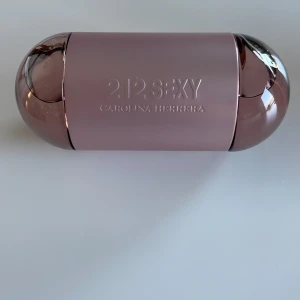 212 Sexy Eau de Parfum från Carolina Herrera - Säljer en elegant 212 Sexy Eau de Parfum från Carolina Herrera. Flaskan har en unik design med två sfäriska delar i en rosa metallisk nyans. Förpackningen är stilren och matchar flaskans färg. Perfekt för den som vill ha en sofistikerad och sensuell doft.