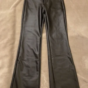 Snygga svarta trendiga skinnbyxor från Calzedonia - Snygga svarta byxor i syntetmaterial från Calzedonia. De har en högmidjad design med en knappdetalj framtill. Byxorna är flare och jätte snygga!! Aldrig använda och helt nya. Säljs då de är för långa tyvärr💕 Trendiga och är slutsålda💕💕