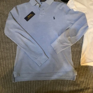 Ljusblå pikétröja från Ralph Lauren - Säljer en stilren ljusblå pikétröja från Ralph Lauren i storlek XS. Tröjan har långa ärmar och en klassisk krage med knappar. Den ikoniska loggan är broderad på bröstet. Perfekt för en avslappnad men ändå elegant look. Pris kan såklart diskuteras. Fråga om du har funderingar.