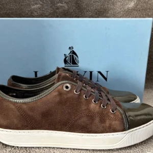 Bruna  Lanvin - Snygga bruna sneakers från Lanvin i mocka med glansiga detaljer. De har en vit sula och snörning framtill. Perfekta för en stilren look, både till vardags och fest. Skorna är i mycket bra skick. Inget og tillkommer! Skorna har små defekter på toecapen som it syns vid andvändning. Uk 5 passar 41-42