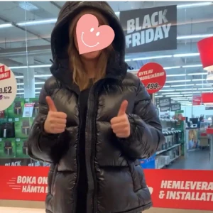 Svart pufferjacka med huva - Säljer en svart pufferjacka med huva. Jackan har en glansig yta och dragkedja framtill. Perfekt för kyliga dagar. 