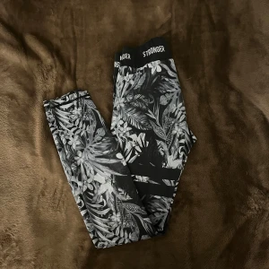 Svarta leggings med blommönster från Stronger - Snygga svarta leggings från Stronger med ett stilrent blommönster i grått och vitt. Perfekta för träning eller en avslappnad dag. De har en elastisk midja med logotypen 'STRONGER' orginal pris 799!!