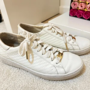 Vita sneakers med gulddetaljer michael kors - Snygga vita sneakers från Michael Kors med gulddetaljer på snörningen. Skorna har en texturerad yta och klassisk snörning. Perfekta för en stilren look.