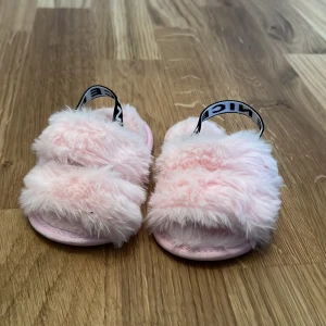 Rosa fluffiga sandaler med blommönster - Söta rosa sandaler med fluffigt pälsmaterial och elastiska band med text. Sulan har ett fint blommönster som ger extra charm. Perfekta för en mysig och lekfull stil.