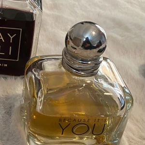 Parfym Because It's You - Elegant parfymflaska med en rundad silverfärgad kork. Flaskan är genomskinlig och innehåller en gyllene doftvätska. Texten 'Because It's You' syns på framsidan.