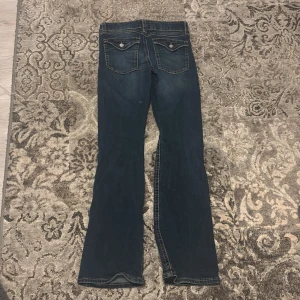 Blå bootcut jeans - Snygga blå bootcut jeans med klassisk femficksdesign och dekorativa sömmar på bakfickorna. Perfekta för en avslappnad stil.