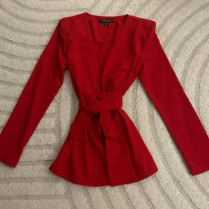Röd kavaj  - Snygg röd kavaj  med knytband i midjan. Den har en v-ringad design och långa ärmar, storlek S