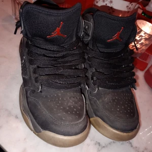 Nike Air Jordans mars - Säljer ett par svarta Nike Air Jordans med röda detaljer. Skorna har snörning och en hög design med perforerade detaljer för ventilation. Den ikoniska Jumpman-loggan syns på plösen och hälen.