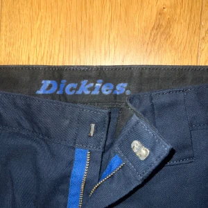 Mörkblå byxor från Dickies - Säljer ett par mörkblå byxor från Dickies i bra skick. De har en klassisk design med dragkedja och knapp framtill. Perfekta för både vardag och arbete. Byxorna har en normal passform.