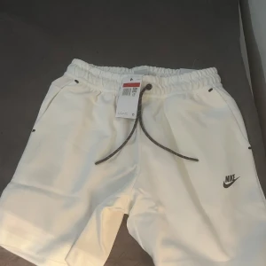 Vita shorts från Nike - Säljer ett par vita shorts från Nike i nytt skick. De har en bekväm elastisk midja med snörning och är perfekta för sommarens alla aktiviteter. Shortsen har en klassisk design med Nike-loggan på benet. Perfekta för både träning och avslappnade dagar Köpt är köpt lämna ej tbx 