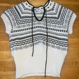Vit och svart stickad tröja från Zara - Säljer en superfin vit och svart stickad tröja från Zara. Den har ett snyggt mönster och en v-ringad hals med snörning. Tröjan är kortärmad och perfekt för både vår och höst. Den är i bra skick och redo för en ny ägare!