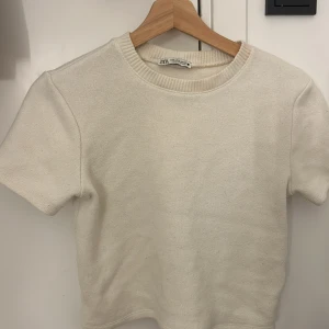 Vit kortärmad tröja från Zara - Säljer en stilren vit kortärmad tröja från Zara i storlek S. Tröjan är i ett mjukt material och har en rund halsringning. Perfekt för en avslappnad vardagslook eller att klä upp med accessoarer. 