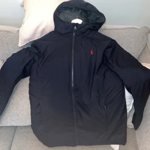 Svart jacka med huva från Polo Ralph Lauren - Snygg svart jacka från Polo Ralph Lauren med huva och dragkedja. Jackan är inprincip helt ny har använt den 1 gång snabbt men inte min stil riktigt köptes för 3500+ säljer snabbt för 2000