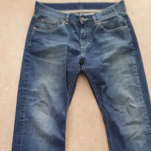 Säljer ett par klassiska blå jeans från Dressmann i storlek W34 L32. De är tillverkade i 100% bomull och har en snygg, lite sliten look. Perfekta för vardagsbruk med en normal passform och traditionell design med fem fickor och knappgylf.